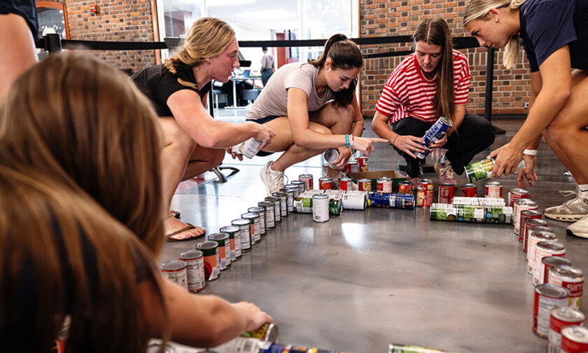 Womens lacrosse players surround stacks of cans in a rectangle