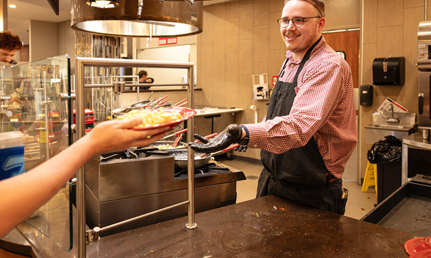 Gray Stone passes a plate to a student on the cafeteria serving line