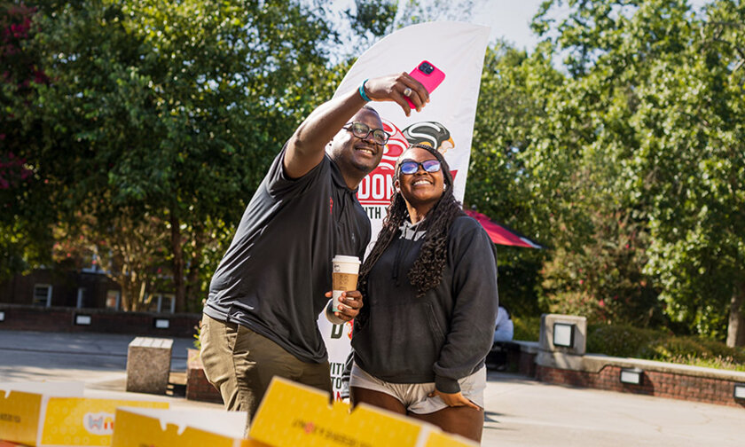 Harry Titus takes a selfie with a student in front of the Donuts with the Dean banner