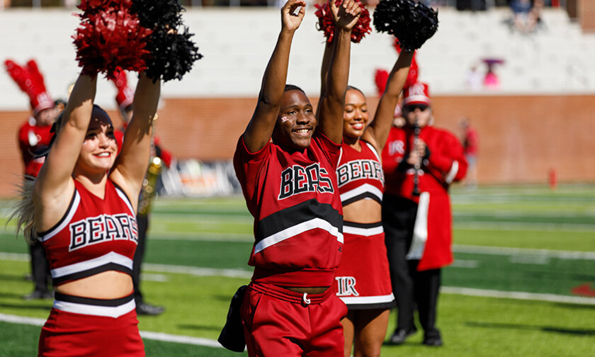 Four members of the spirit team raise their hands on the field