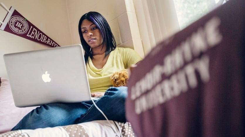 Student works on laptop on bed in dorm room