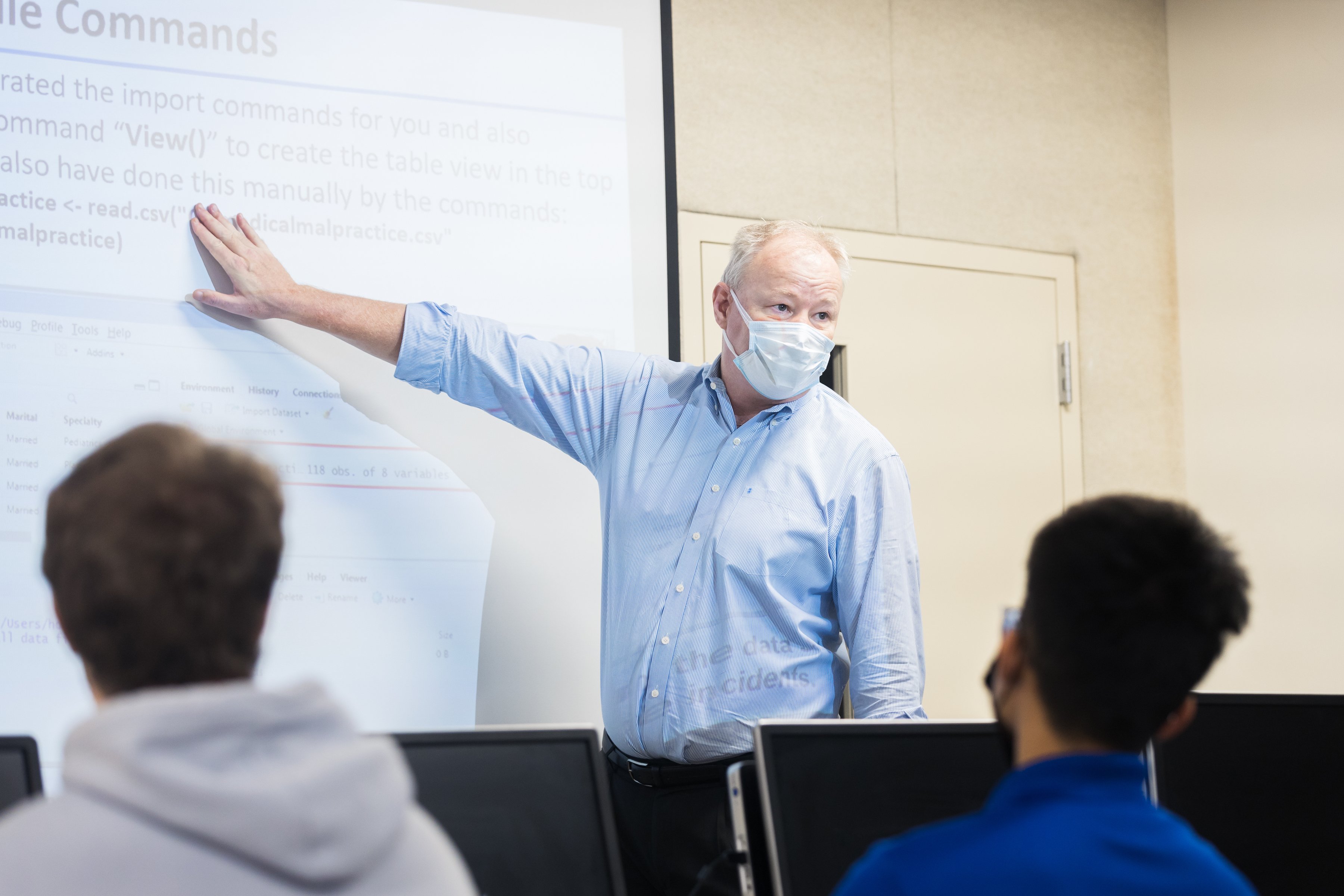 Bjarne Berg, Ph.D., stands in front of a white board while teaching a class indoors and wearing a mask
