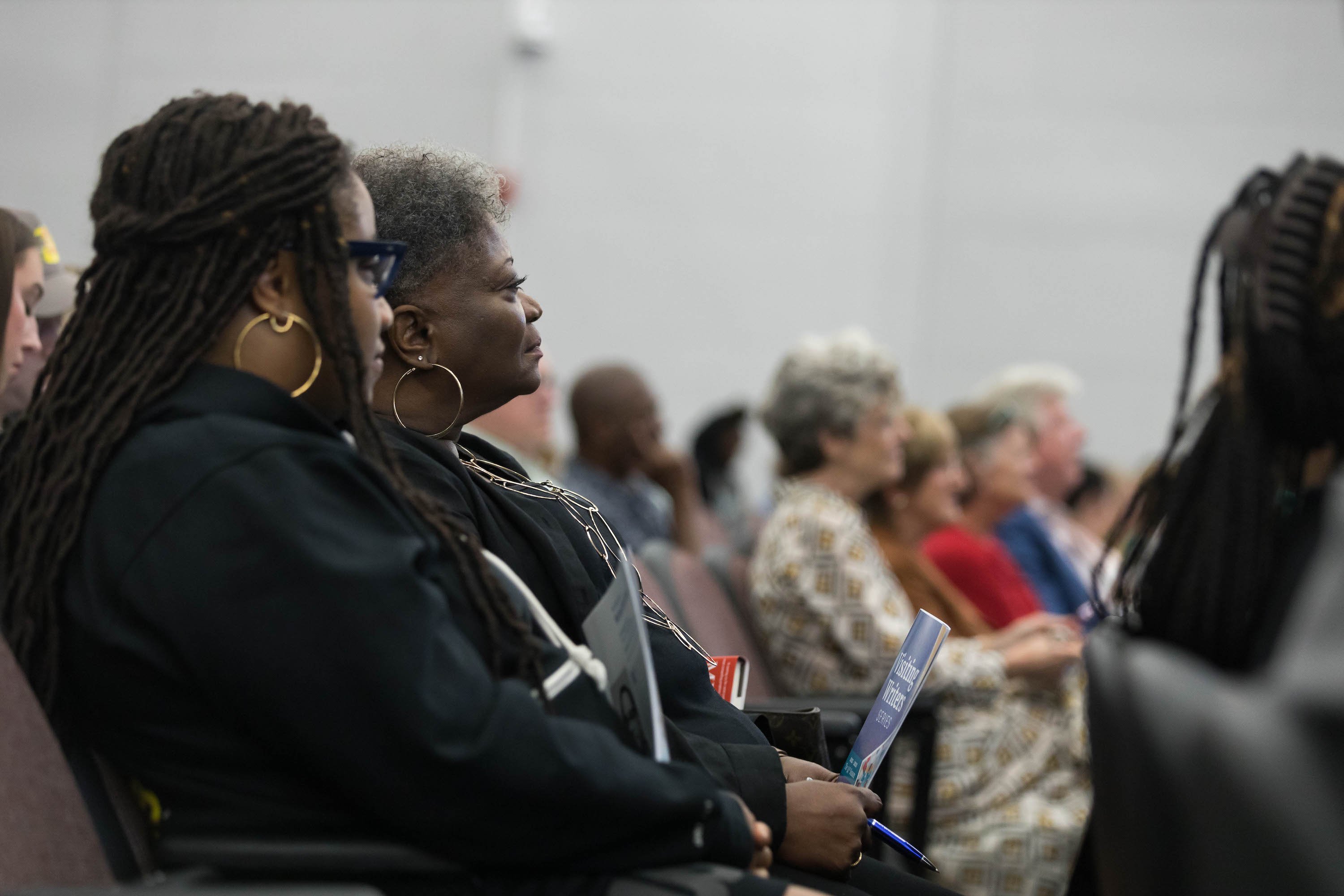 A crowd of people sitting an auditorium face the stage