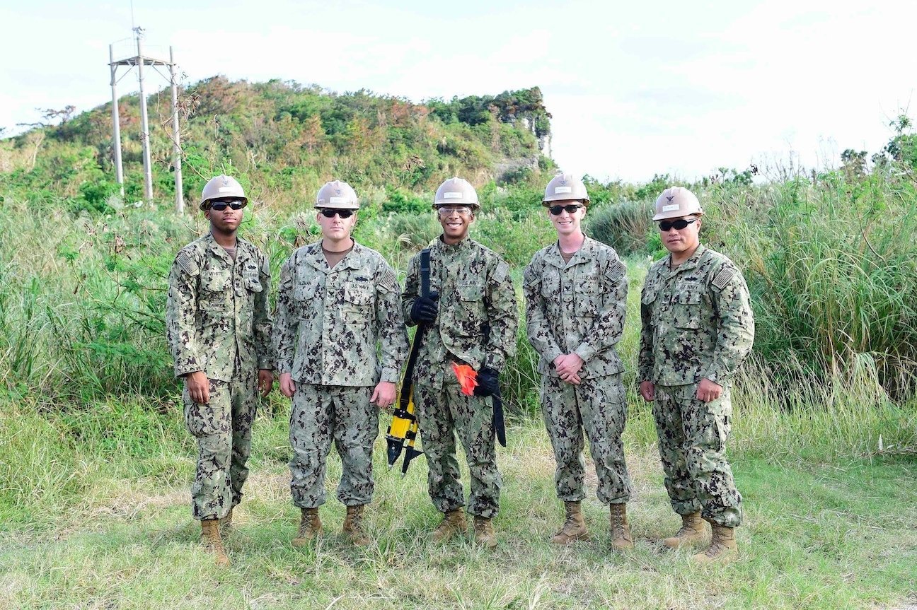 Five men in U.S. Navy fatigues stand together outside