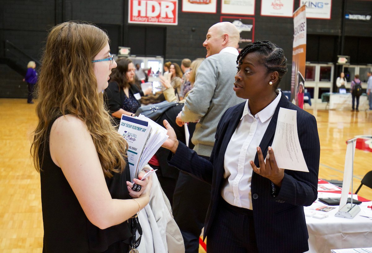 Two people chat at a career fair inside a gym