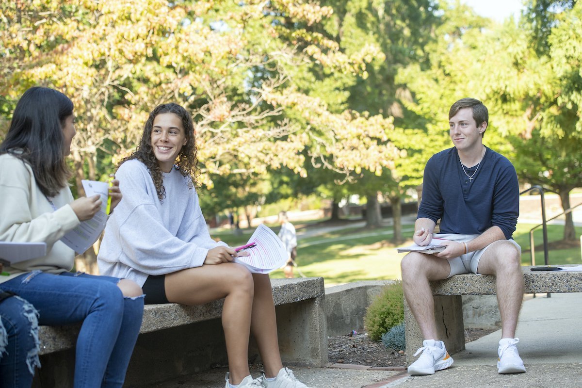 Three students sit outside and talk