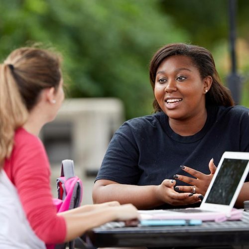 Two female students working outside on class assignment at table