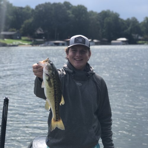 A student stands on a boat and holds out a fish to the camera