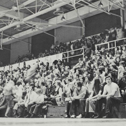 A group of students watch a basketball game indoors in a black and white 1973 archive photo