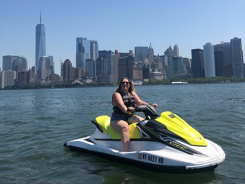 Milly Treu riding a jet ski with the New York City skyline in the background.