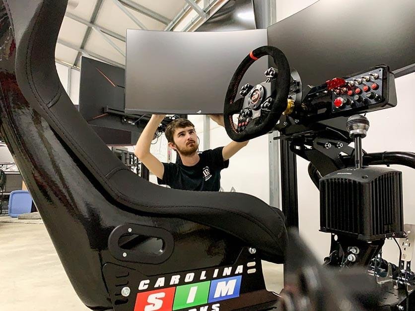 Logan Traxler installs a monitor on a NASCAR simulator