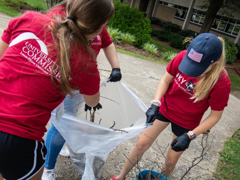 Three student volunteers clean up yard debris as part of a community service project.