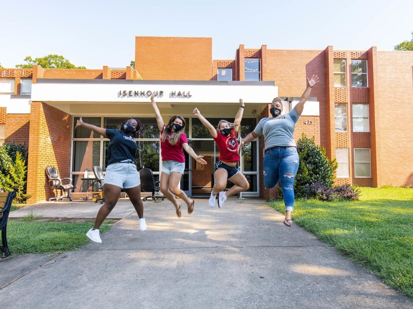 Four students jump into the air in front of Isenhour Hall. 