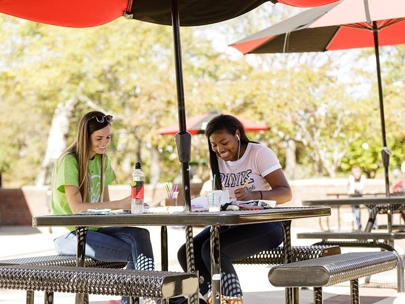 Students laughing and studying under an umbrella in Shaw Plaza