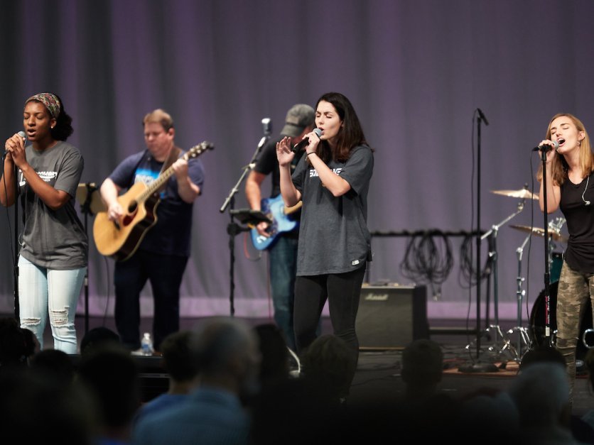 Students sing into microphones on a stage