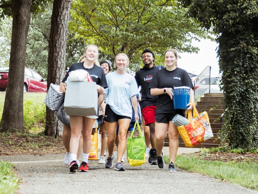 Students carry bags and boxes to a dorm during move-in.
