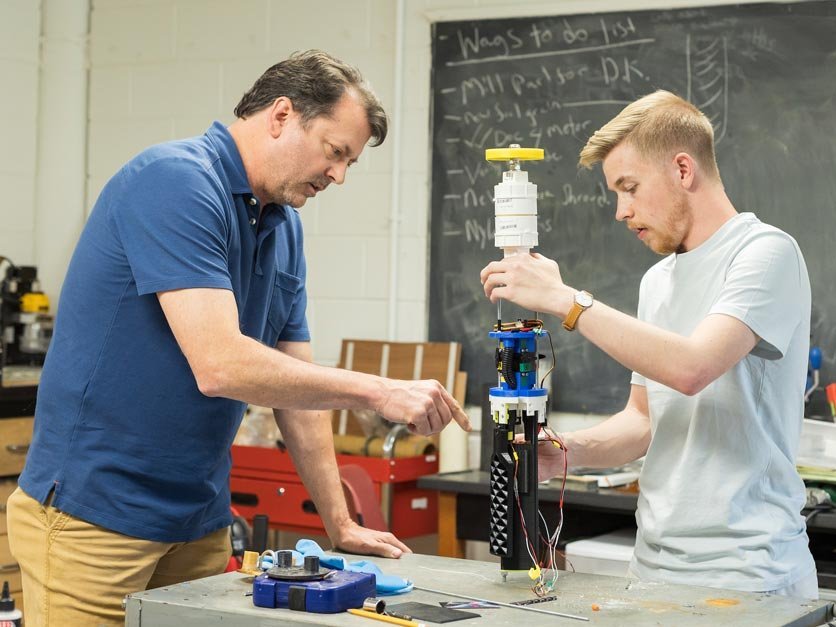 Professor and student work on rocket design in classroom