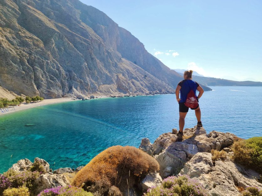 On a coastal hike, Chrissy Elliott stands with her back to the camera overlooking the Loutro Bay in Crete, Greece.