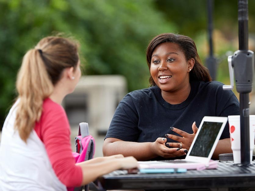 Two female students working outside on class assignment at table