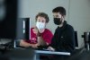 Two masked students sit in a classroom and look at the same computer screen