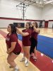 Three women stand in a gym and braid their hair