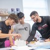 Three men work together assembling a project in a lab