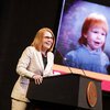 Summer McGee at a podium with a childhood portrait projected on screen in background
