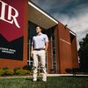 Brooks Higginbotham in front of PE Monroe Auditorium and LR banner