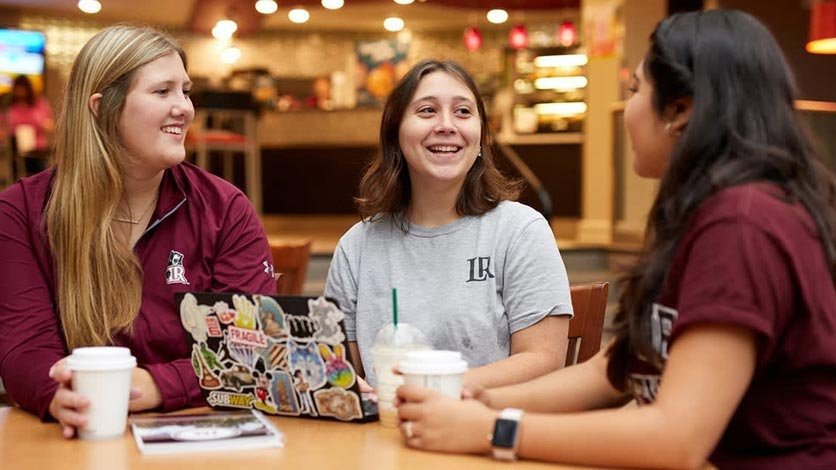 THree students around a table talking in the coffee shop