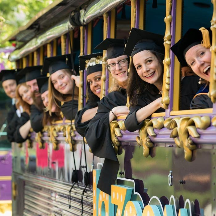 Graduate students smiling on trolley on way to commencement ceremony