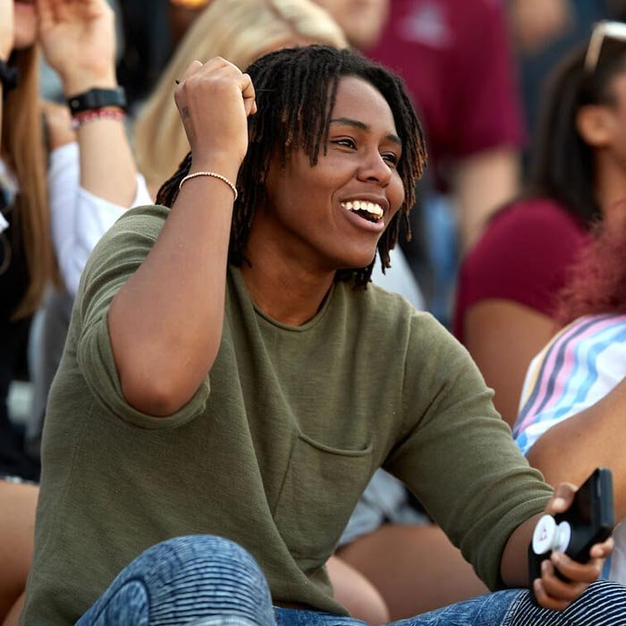 Student cheering football team in stands with arm raised