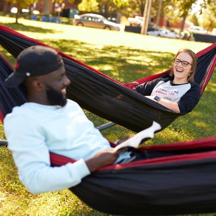 Two students laughing while studying in hammocks on lawn