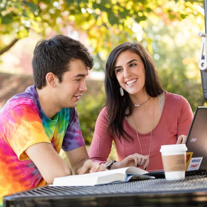 Two students talking at table outside