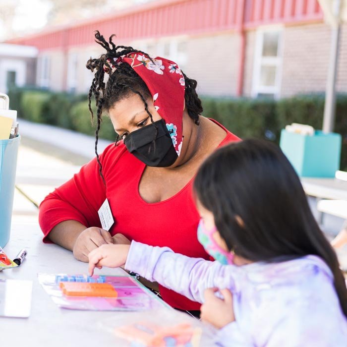 A student works with a child at an outside table